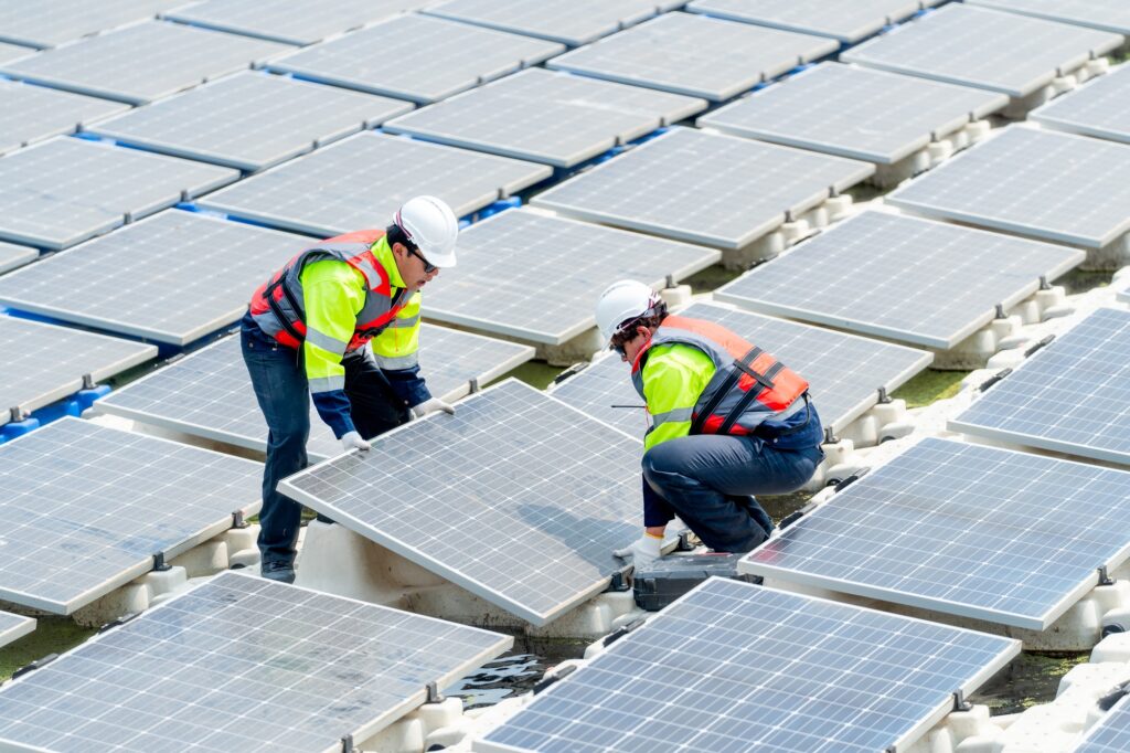 Side view of two technician workers help to install or set up solar panels over water reservoir