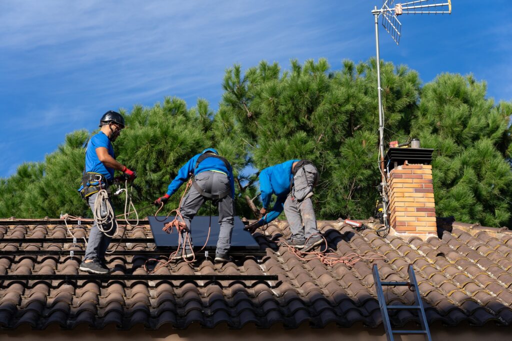 Three solar panel installation technicians installing solar panels on a roof of a house